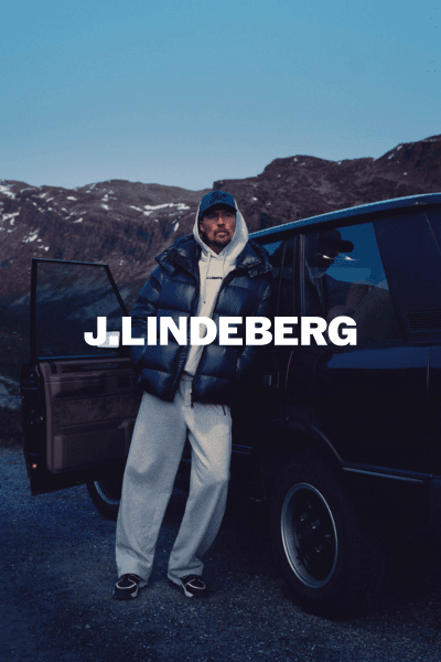 Bannerbilde for J. Lindeberg med modell i dunjakke og hettegenser ved bil i naturmiljø